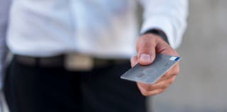 A person in business attire holding an Amex Business Platinum credit card.