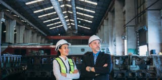 A business owner and an employee wear protective gear and inspect a workplace for risk assessment