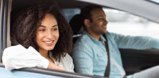 View from the passenger side window of two people in a car.