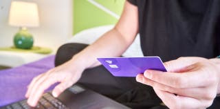 A person holding a credit card in their hand and typing on a laptop.