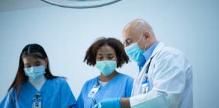 Three masked medical professionals in medical scrubs stood together