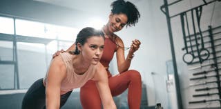 A woman is doing a plank while her personal trainer holds a stopwatch, coaching her from behind