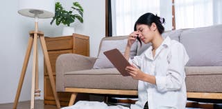 A woman in her living room exhibits stress over cancelling her trip while using a tablet.