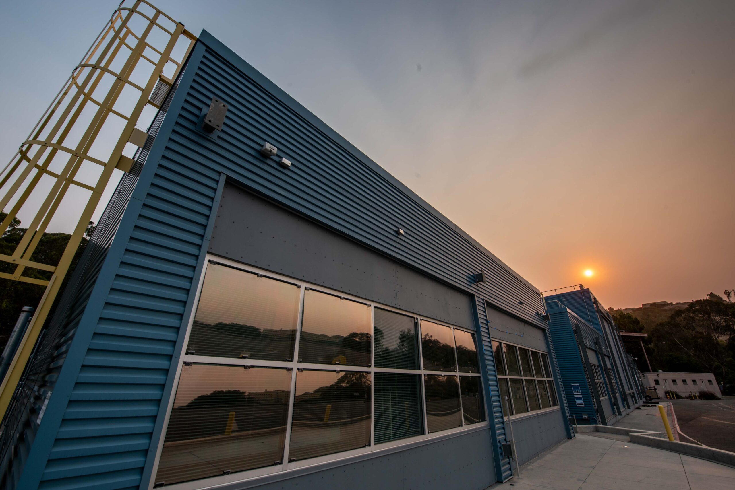 The sun obscured behind smokey skies over a blue building.