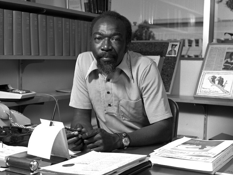 Black and white portrait of James (Jim) Harris sitting behind his desk.