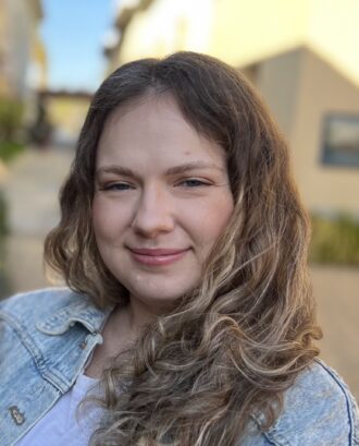 Anastasiia Butko, a person with medium-length brown hair wearing a jean jacket over a white top.