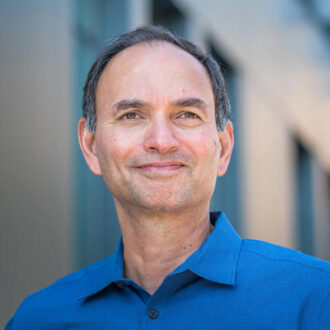 Nitash Balsara, a person with short gray hair wearing a blue collared shirt, photographed outdoors next to a building.