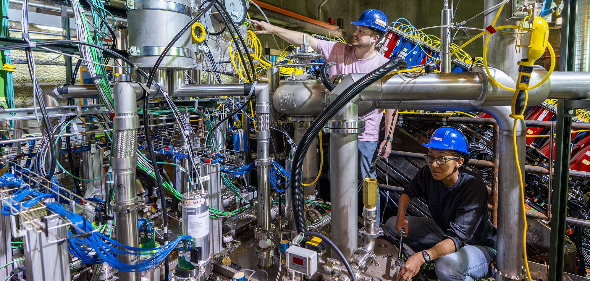 Two scientists in hard hats working on the 2x2 prototype detector for the DUNE near detector.