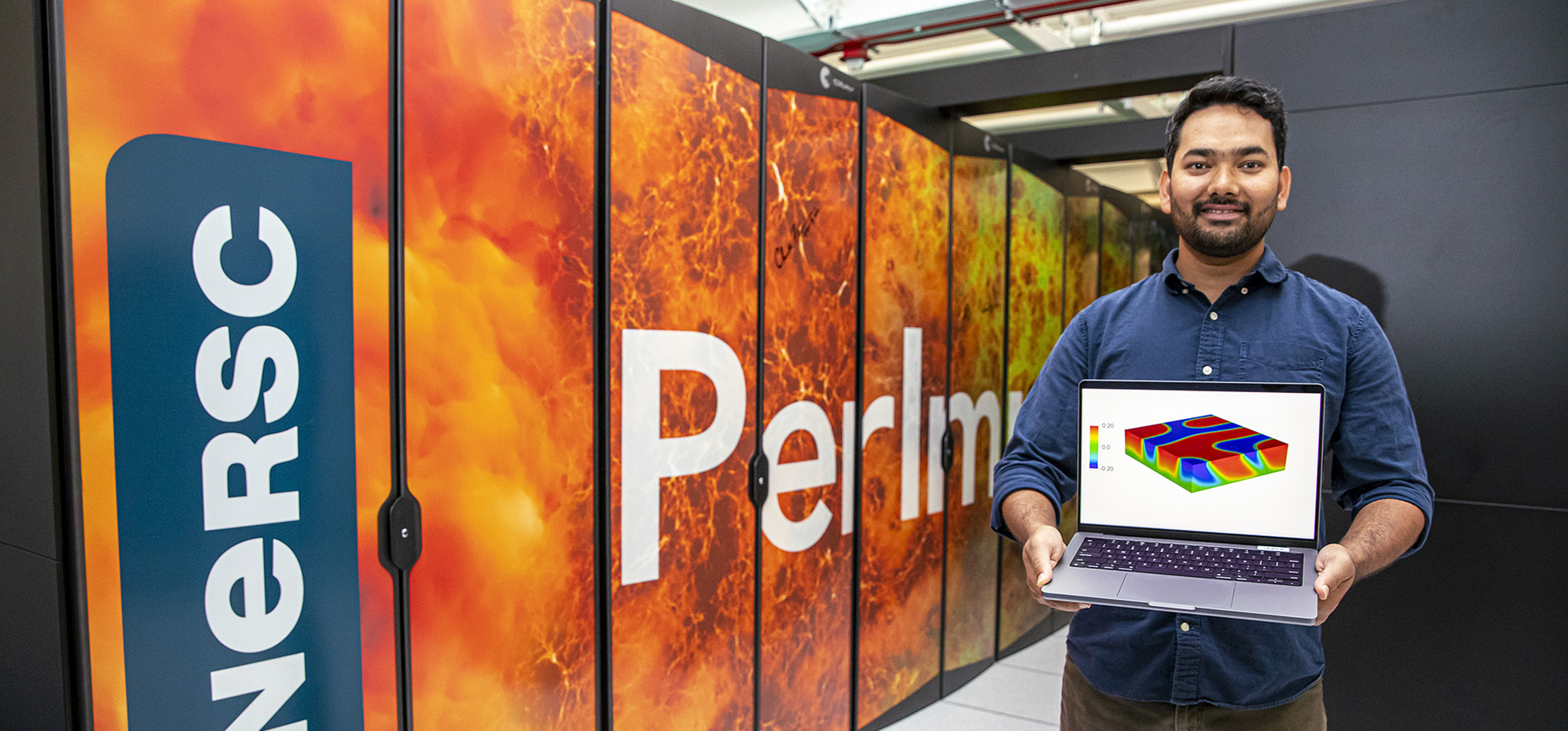 Prabhat Kumar holding a computer with a simulation in front of a super computer.