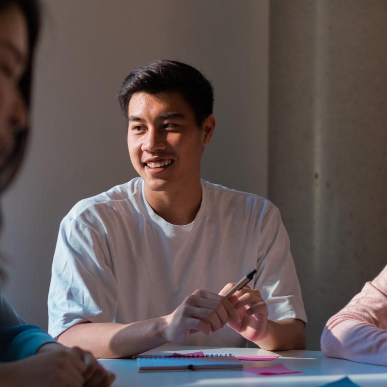 Student sitting at a desk holding a pen and smiling