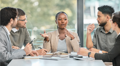 Five individuals in a meeting with the woman in the middle talking to the group