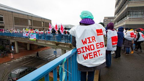 Menschen mit Verdi-Warnstreik-Westen stehen vor dem Gebäude I2 des MHH-Campus.