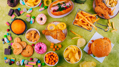 Viele ungesunde Speisen wie Donuts, Pommes, Weingummi und Burger stehen auf einer grünen Oberfläche. 