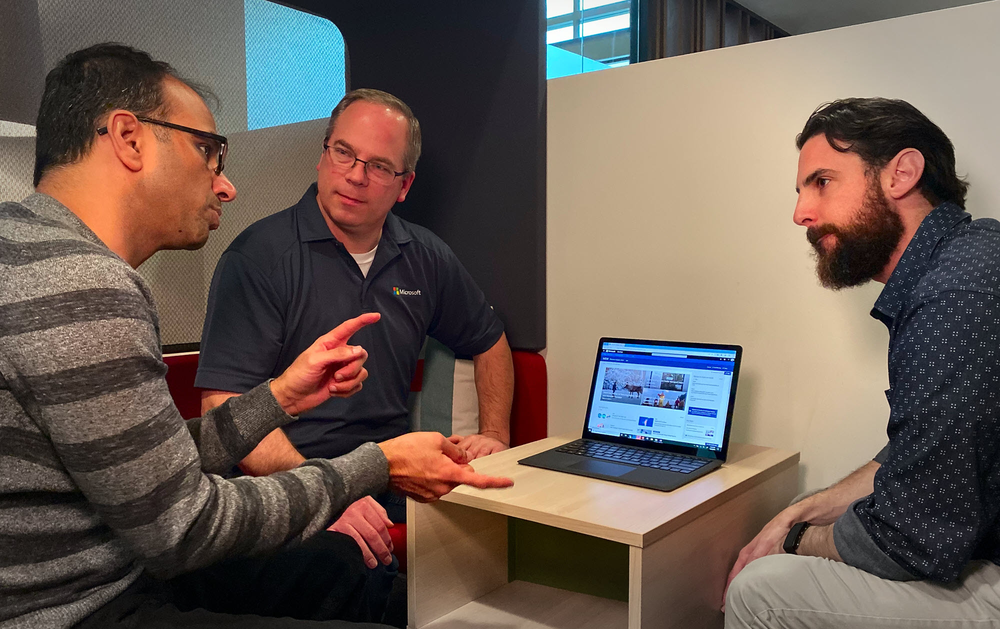 Padur, Crewdson, and Jaffe chat while sitting on a couch in a public gathering spot on the Microsoft campus. They are talking over a laptop that is open to the MSW home page.