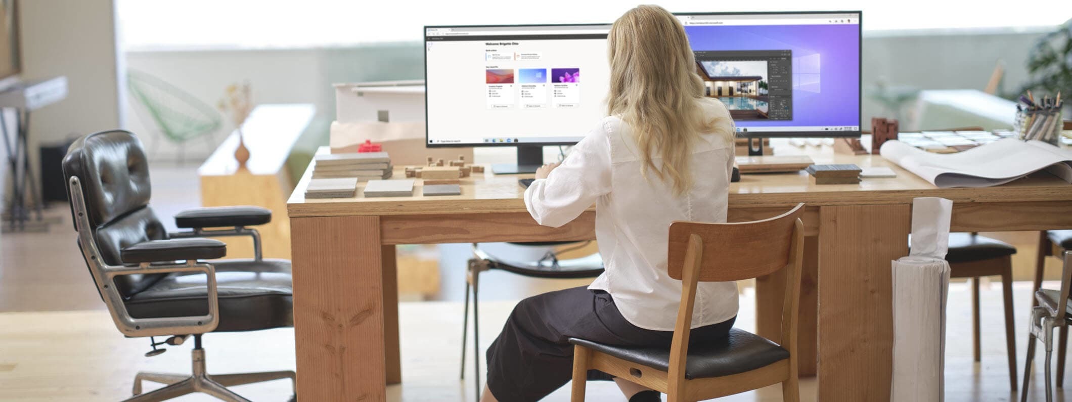 A female architect sitting at an office desk showing Windows 365 and its Welcome screen on dual desktop monitors.