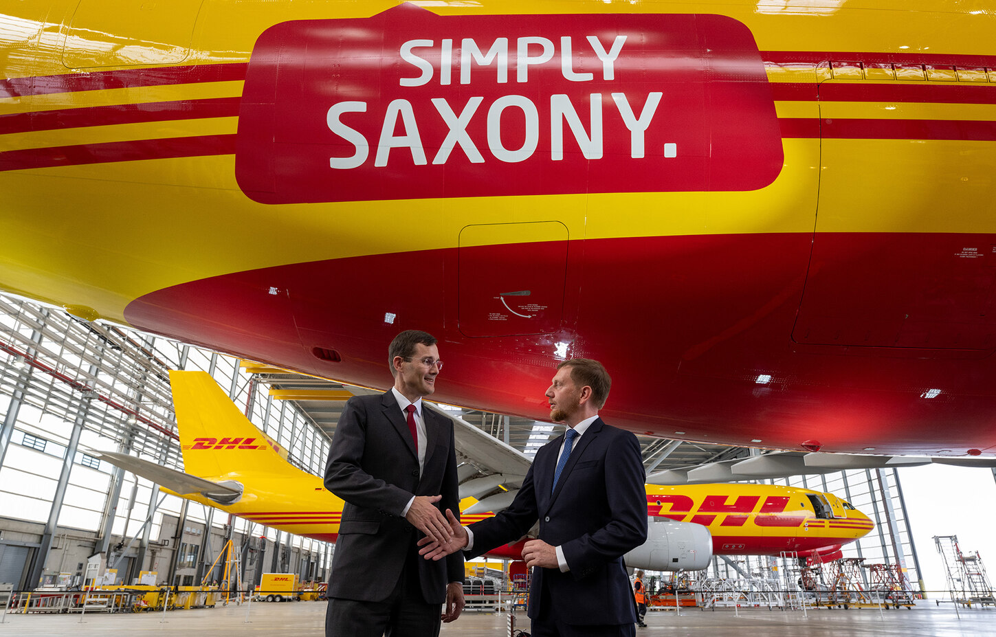 Zwei Männer stehen vor einem Flugzeug in einem Hangar und reichen sich die Hand.