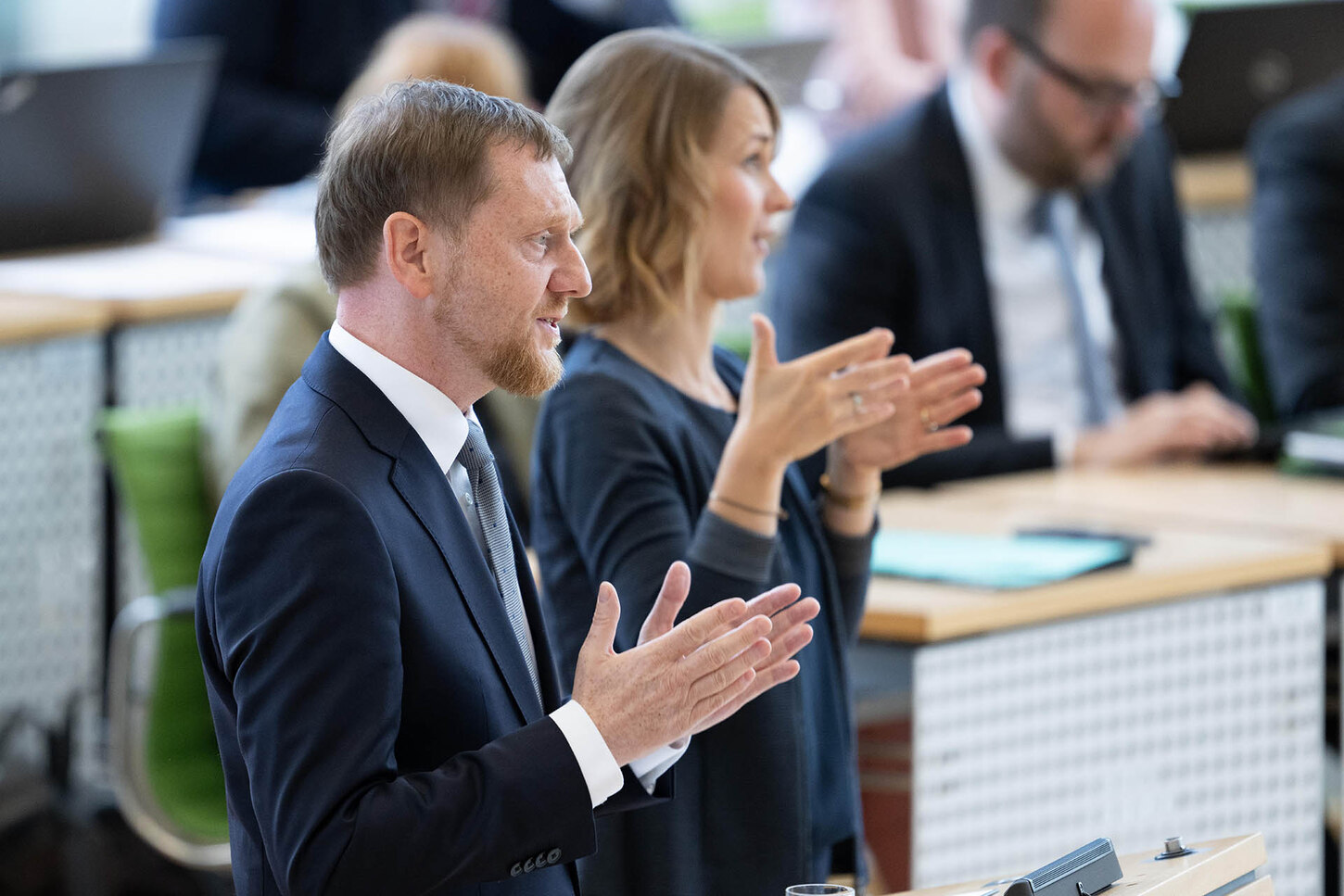 Ein Mann gestikuliert an einem Rednerpult. Im Hintergrund steht eine Gebärdesprache sprechende Frau.