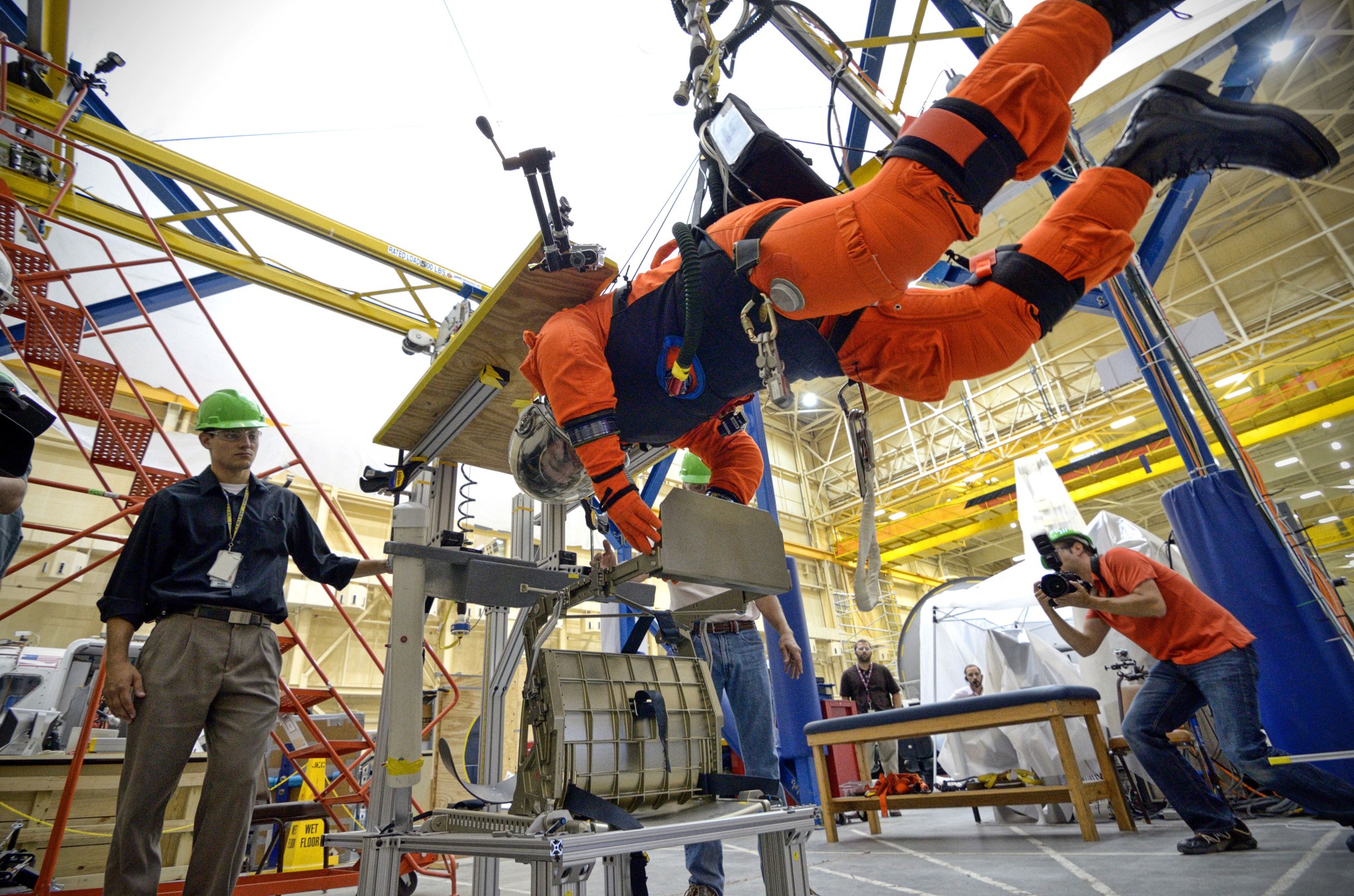 Astronaut hanging in harness in a flight suit to evaluate the amount of dexterity the suit would provide for various tasks including translating across handrails, working with tools, and entering a spacecraft hatch.