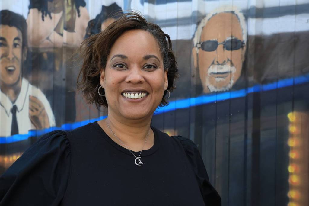 Public Affairs Officer Tiffany Fairley stands in front of a mural and smiles at the camera at NASA's Kennedy Space Center. 