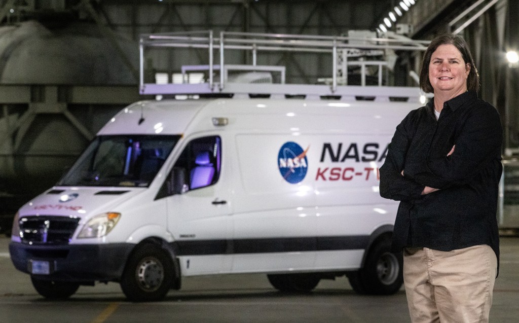 Transportation Officer Melissa Coleman stands in front of a white van with the NASA emblem on it.