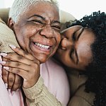 Adult daughter kissing smiling mother.