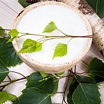 Xylitol crystals in a birch bowl beside a birch branch with leaves.