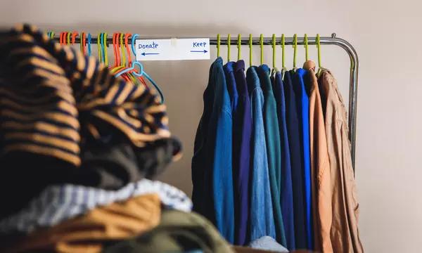 Clothes rack. Sign in middle. Left pointing arrow says Donate with clothes hanging. Right facing arrow says "keep" pointing to other clothes.