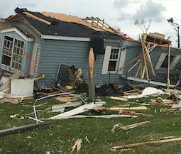 a house with blue siding is partially destroyed, likely by a tornado