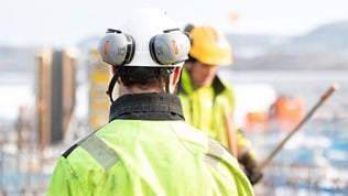 Illustrasjonsbilde: Mann med hjelp og hørselvern sett bakfra på byggeplass. 