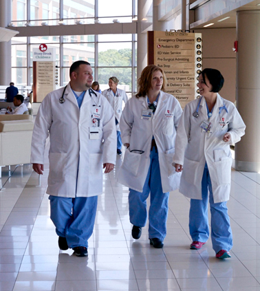 Three Stony Brook Medicine personnel walk through the Hospital as they talk amongst each other