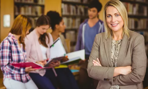 Professor looking at camera with arms folded in library