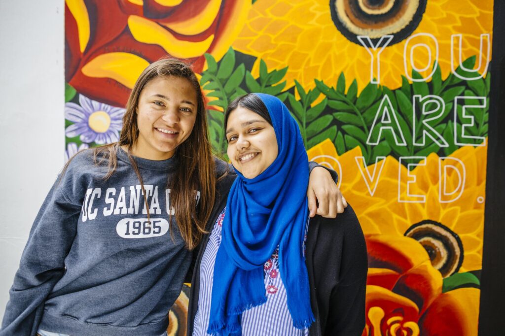 Two student smiling in front of a mural