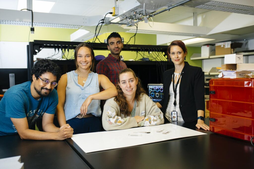 5 people in a lab standing around a table smiling.