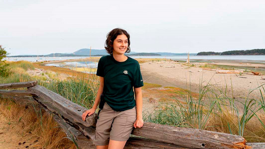 A student sits on a fence in front of a beach.