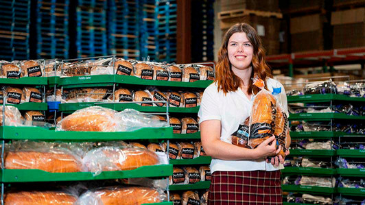 A student stands in the Portofino bakery holding a bag of bread.