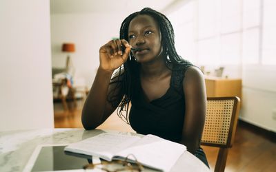 Student learning at home. African woman sitting at home and writing homework.