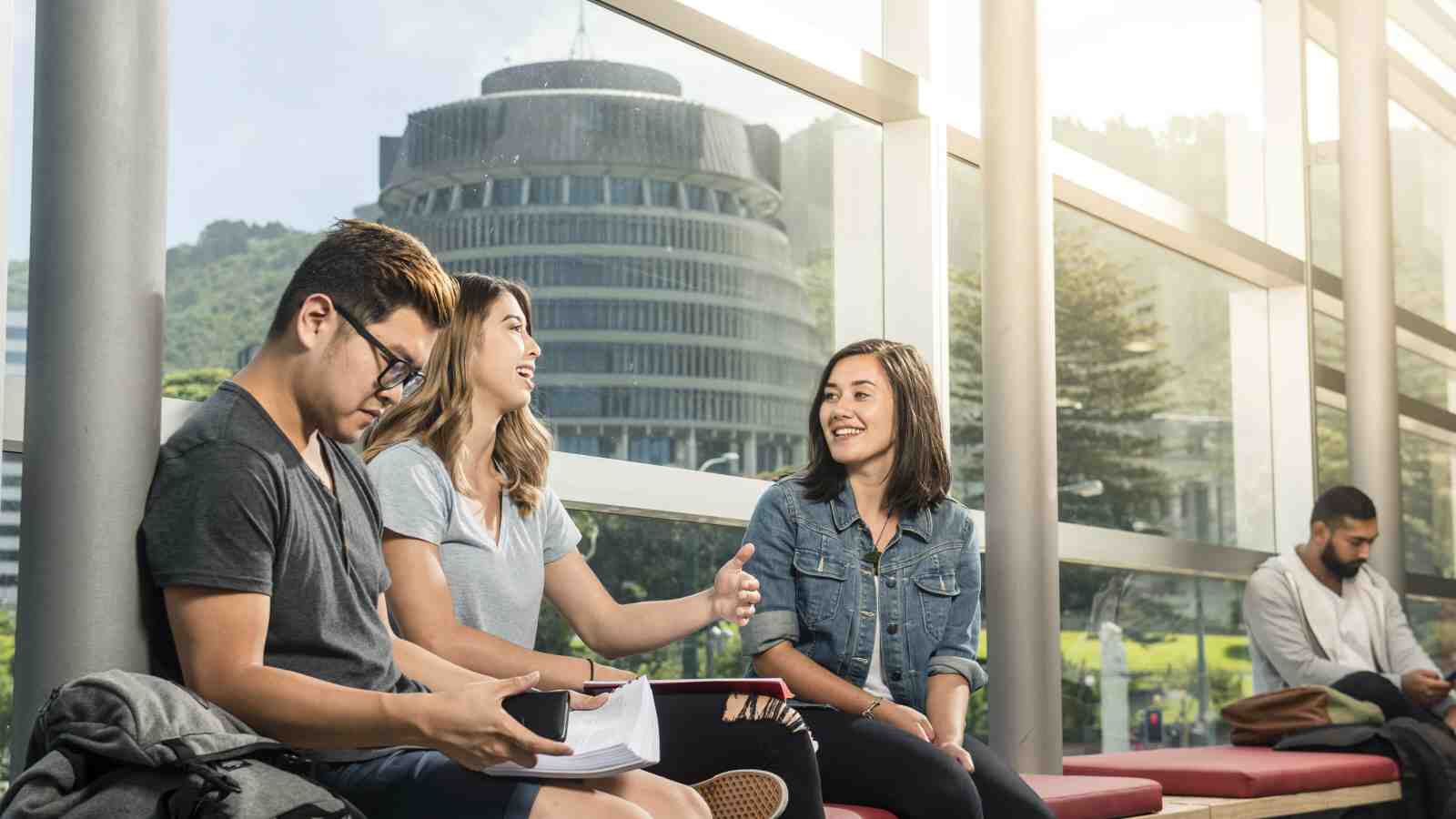 A group of students sitting and talking at Victoria University's Pipitea campus with the Beehive (Parliament buildings) in the background.