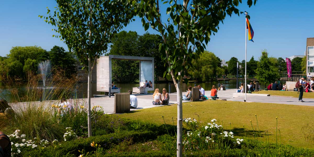 Landscape photograph of the campus, showing students relaxing on a sunny day with the LGBTQ flag raised